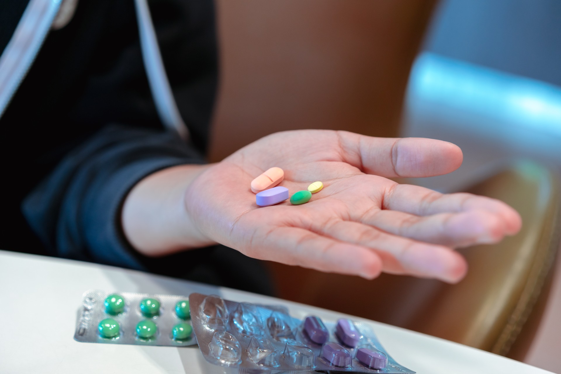 Hand holding out prescription medication drugs and pills in various shapes and colours for treatment